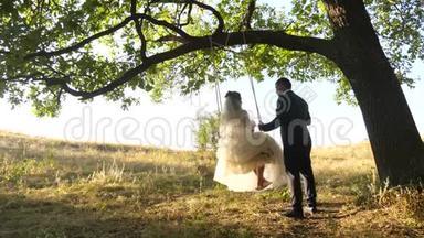 新娘和新郎在公园里荡秋千。 幸福的一对相爱的夫妻在森林里荡秋千